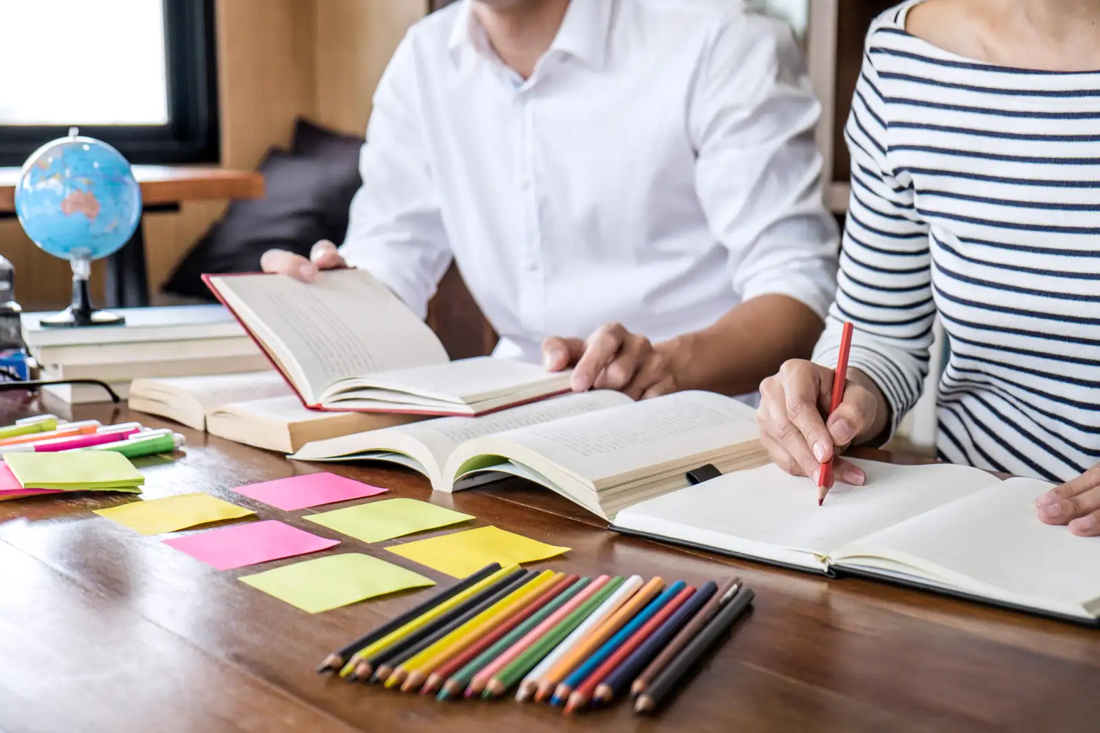 Two people studying together over the same open books and lesson notebook